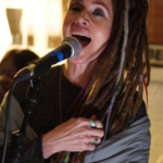 Heatherlyn sings into a microphone at rehearsals. Belinda Kae is partially visible in the background.