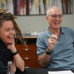 Heatherlyn and Steve Bassett laugh together during a virtual interview. Heatherlyn is on the left in the foreground whilst Steve appears out of focus in the background to the right.