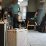 Two tour suitcases in focus in the foreground, with one person stood and one person sat in the background out of focus.