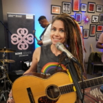 Heatherlyn smiles and looks at the camera. Marcus Copeland, Tony Bean and Ben Okafor prepare for the gig in the background.