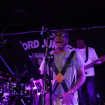 Ben Okafor sings whilst playing a drum at Record Junkee. Marcus Copeland, Tony Bean and Steve Bassett are partially visible in the background.