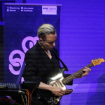 Rich Wilson playing guitar, with Martin Trotman and Marcus Copeland partially in view.