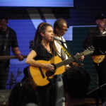 From right to left, Tony Bean is playing bass guitar, Heatherlyn sings and plays an accoustic guitar, Ben Okafor plays a drum and Steve Bassett plays on an electric guitar.